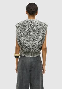 Strikket ærmeløs top i sort og hvid med et tekstureret mønster og ribbet kant. Kombineret med løse grå bukser og tilbehør.