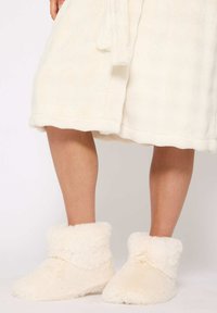 Zapatillas de casa de color crema, suaves y esponjosas, con un puño doblado y una textura suave, de diseño de punta redonda, que se llevan con una bata de color crema a juego.