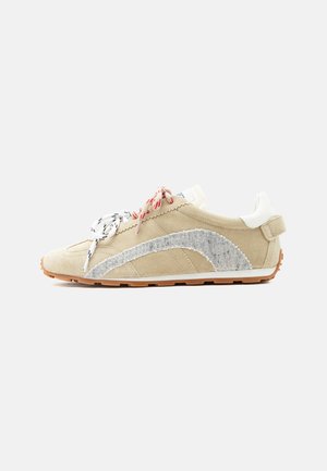 Zapatilla deportiva de ante beige con cordones blancos y rojos estampados, franja lateral texturizada gris, lengüeta trasera blanca y suela de goma marrón.