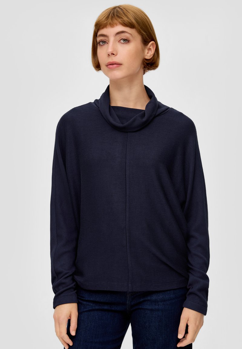 Navy blauwe coltrui met lange mouwen, gemaakt van een textuurstof en met een ontspannen pasvorm, gecombineerd met donker denim jeans.