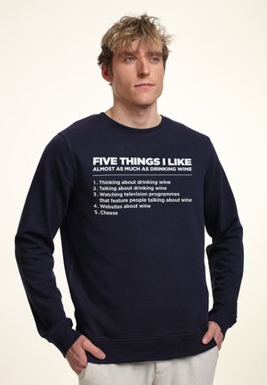 Granatowy sweter z białym napisem przedstawiającym pięć zainteresowań. Okrągły dekolt, długie rękawy, ściągacze przy mankietach i u dołu, wykonany z miękkiego materiału.