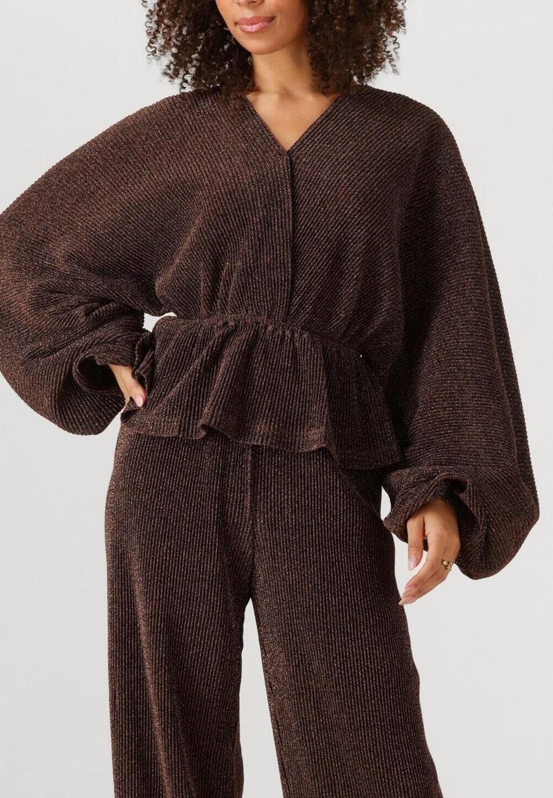 Een bruin, geribbeld stoffen top met een peplum taille, oversized mouwen en een V-hals ontwerp, gecombineerd met bijpassende hooggerokte broek.