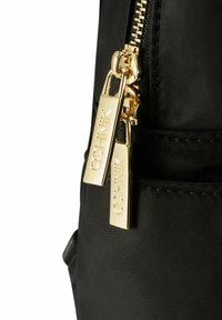 Czarna torba z tkaniny z złotym zamkiem błyskawicznym z dwoma uchwytami, na każdym z nich wygrawerowana nazwa marki, podkreślająca elegancki design i trwały materiał.