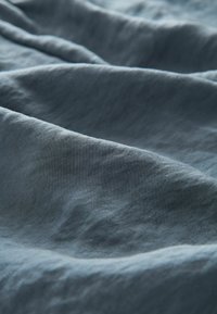 Weiche, leichte Stoff in einem gedämpften Blauton, der eine glatte Textur mit subtilen Wellen und Falten aufweist.