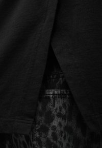 Κοντινή λήψη μαύρου υφάσματος που επικαλύπτει γκρι τζιν με λεοπάρ σχέδιο και εμφανείς λεπτομέρειες ραφής.