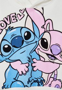 Felpa bianca con personaggi dei cartoni animati colorati: una creatura blu con grandi occhi e una creatura rosa, entrambe sorridenti, circondate da cuori.