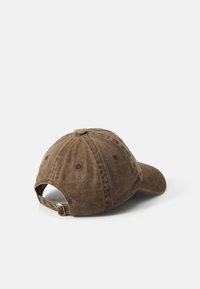 Brown cotton baseball cap with a curved visor, adjustable strap, and six-panel design featuring visible stitching and ventilation eyelets.
