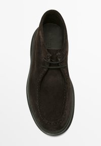 Brauner Wildlederschuh mit runder Kappe, zwei Ösen für Schnürsenkel, kontrastierenden Nähten und einer Gummisohle. Durchgehend glatte Textur.