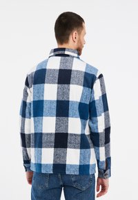 Camicia di flanella a quadri blu e bianca con colletto, polsini a bottone e una texture morbida. Il motivo presenta grandi quadrati in diverse tonalità di blu.