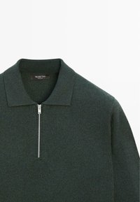 Tmavě zelený pletený svetr se zapínáním na zip vpředu, plochým límcem a texturovanou látkou. Obsahuje jemný vzor a značkový štítek uvnitř u krku.