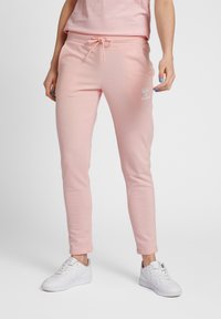 Rosa joggers i mjukt material med en åtsittande design, elastisk midja, dragsko och logodetalj på låret, kombinerat med vita sneakers.