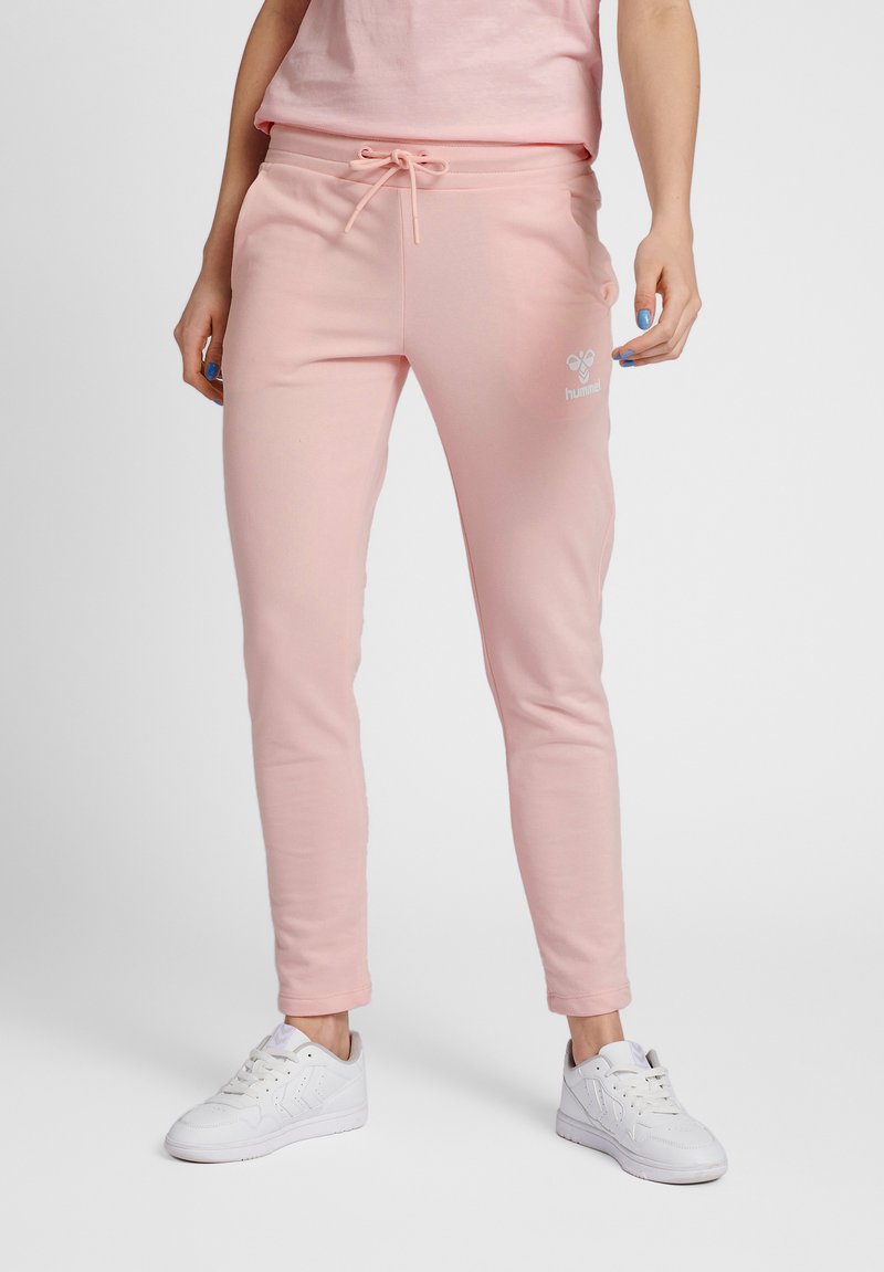 Rosa joggers i mjukt material med en åtsittande design, elastisk midja, dragsko och logodetalj på låret, kombinerat med vita sneakers.