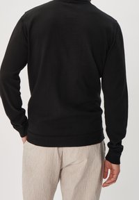 Pull noir à manches longues avec un ourlet et des poignets côtelés. Le tissu semble doux avec une texture lisse, conçu pour un look ajusté au dos.