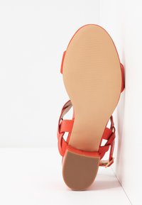 Sandales rouges avec une semelle texturée, dotées de brides ajustables et d'un design élégant. La vue arrière met en valeur la bride et le détail de la couleur.