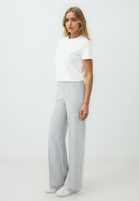 Weiße Baumwoll-T-Shirt, kurze Ärmel, Rundhalsausschnitt, kombiniert mit grauen weiten Jogginghosen mit seitlichen Steppnähten, getragen mit weißen Sneakern.