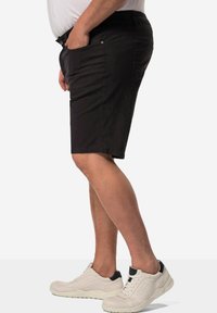 Pantalones cortos de algodón negros con un corte relajado, bolsillos laterales y un dobladillo que cae por encima de la rodilla, combinados con zapatillas blancas y detalles negros.