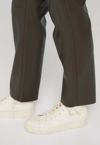 Bruna, högmidjade byxor i konstläder med en slät textur, i kombination med vita snörskor med en strukturerad gummisula.