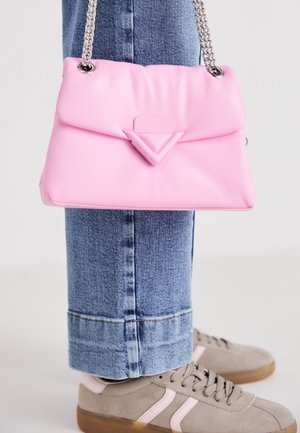 Rosa synthetische Handtasche mit gefalteter Gestaltung, ausgestattet mit einem dreieckigen Akzent und einem silbernen Kettenriemen. Kombiniert mit hellblauen Jeans und Sneakers.