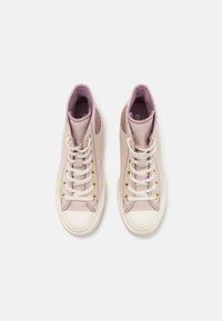 High-top sneakers in soft pink canvas with white rubber toe cap, gold eyelets, and a textured pattern. Pink lining and logo detail on the side.