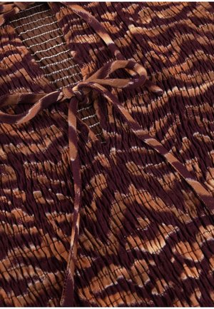 Tissu tie-dye brun et bordeaux avec texture smockée présentant un nœud noué au-dessus d'un panneau en mesh avec des coutures blanches.