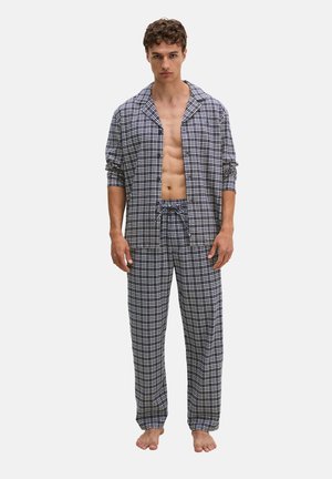 Junger Mann steht barfuß und trägt ein aufgeknöpftes blau-weiß kariertes Pyjama mit langen Ärmeln und passenden Hosen mit Kordelzug.