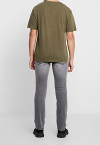 Olivgrön bomullströja med korta ärmar, avslappnad passform och rund hals, i kombination med smala grå jeans och svarta sneakers.