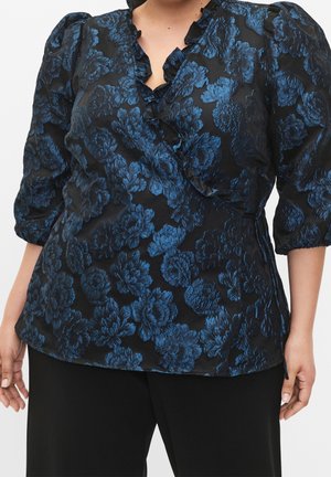 Donna che indossa una blusa avvolgente nera con motivo floreale blu e maniche a palloncino a tre quarti, abbinata a pantaloni neri.