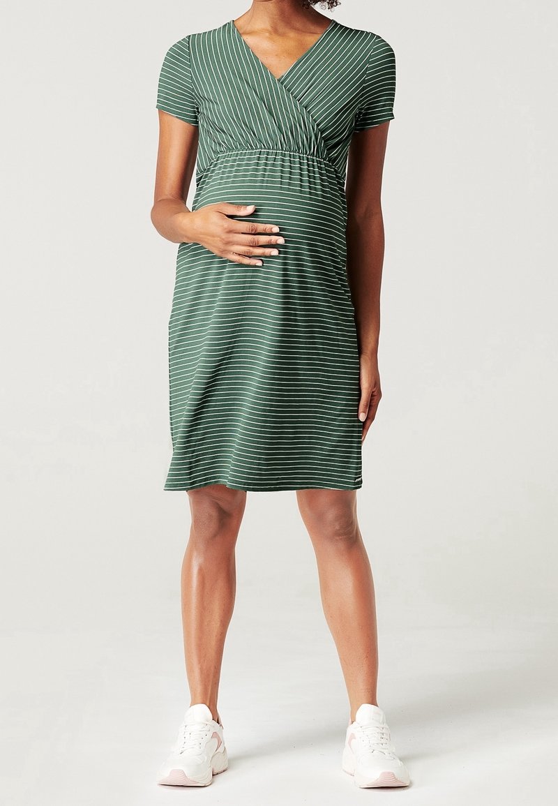 Zelené pruhované těhotenské šaty s krátkými rukávy, výstřihem do V, empírovým pasem a jemnou texturou. Spárováno s bílými teniskami.