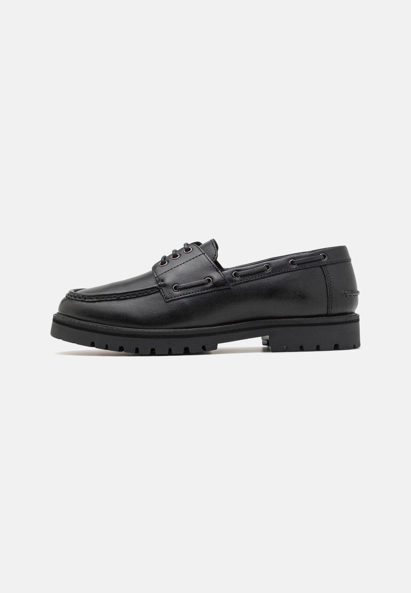 Chaussure bateau en cuir noir avec lacets à l’avant et semelle robuste, vue de profil sur un fond neutre.