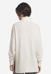 Übergroßer cremefarbener Pullover aus weichem Strickstoff, mit hohem Kragen, gerippten Bündchen und längerem Saum im Rücken.