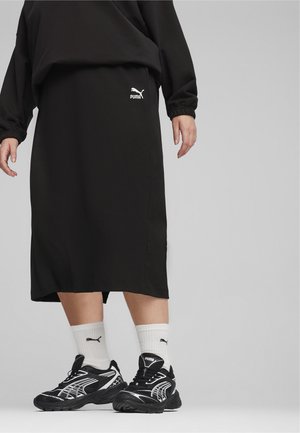 Schwarzer gerippter Strickrock mit einem elastischen Bund und einem weißen Puma-Logo. Kombiniert mit schwarz-weißen Laufschuhen und weißen Socken.