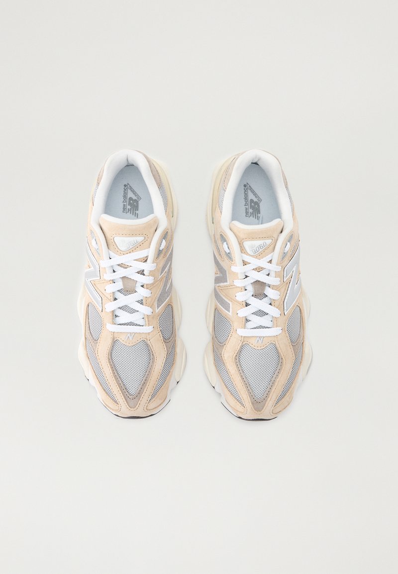 Beige und graue Sportschuhe mit Obermaterial aus Mesh und Wildleder, ausgestattet mit weißen Schnürsenkeln und Logo-Akzenten, die für Komfort und Unterstützung entworfen sind.