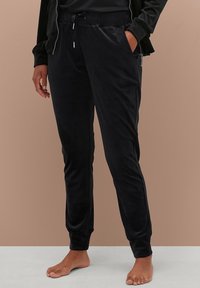 Zwarte, fluwelen joggerbroeken met elastische tailleband, zijzakken en taps toelopende enkels. Glad textuur en zachte stof voor comfort.