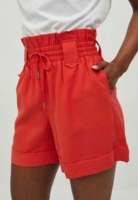 Pantalones cortos rojos de cintura alta con cinturilla elástica, cierre con cordón y dobladillos enrollados. Hechos de tela ligera y suave.