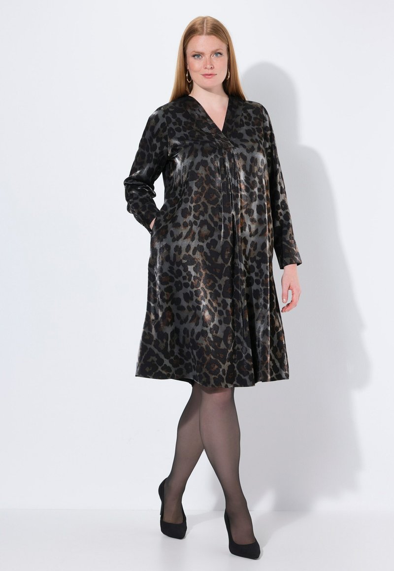 Vestido de estampado de leopardo en tejido brillante, con escote en V, mangas largas y diseño plisado con bolsillos laterales, combinado con tacones altos negros.