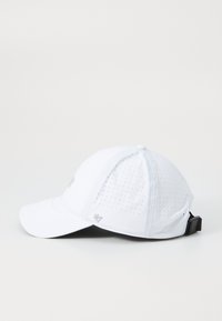 Hvit caps med perforerte paneler for ventilasjon. Har en buet skjerm og et justerbart svart belte bak. Diskrete grå detaljer.