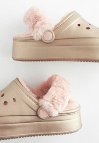 Metallic rose gold platform clogs med rosa faux fur rem og for. Har cirkulære accentknapper og ventilationshuller på overdelen.