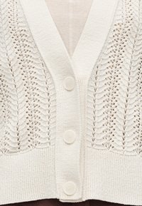 Kremfarget strikket cardigan med bladmønstrete hullmønsterpaneler og tre store, runde knapper foran.