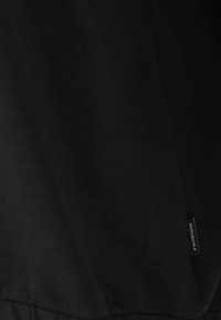 Svart t-shirt i tyg, slät textur, rund halsringning, kort ärm och en liten "Endurance"-tagg på sidsömmen.