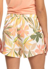 Shorts floraux avec un fond blanc et des motifs de feuilles colorées en rose, vert et jaune. Taille élastique, tissu léger.