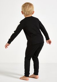 Schwarze Kinderpyjamas mit einem langärmeligen Oberteil, das ein Knochenmuster auf dem Arm hat, und passenden Hosen. Aus weichem, dehnbarem Stoff für hohen Komfort.