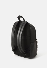 Sac à dos noir avec une finition texturée, présentant une partie supérieure lisse, deux bretelles rembourrées et une poche latérale avec fermeture éclair.