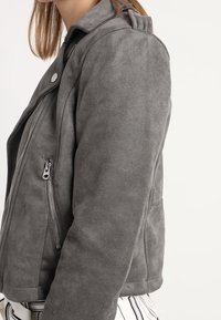 Gray suede moto jacket with a fitted shape, silver zipper details, and a classic collar, featuring a soft texture and minimalistic design.