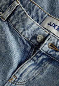 Gaiši zili džinsi ar izbalējušu apdari, detalizēta šūšana, priekšējais rāvējslēdzis un metāla pogas. Uz uzlīmes rakstīts "JJXX."