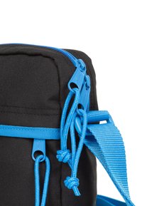 Sort stoftaske med blå lynlåse og stropper; har knyttet detaljer på snore og en glat tekstur. Kompakt design velegnet til at bære genstande.