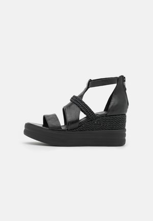 Black wedge sandals with a woven accent, featuring a smooth leather strap design and a thick rubber sole for stability.