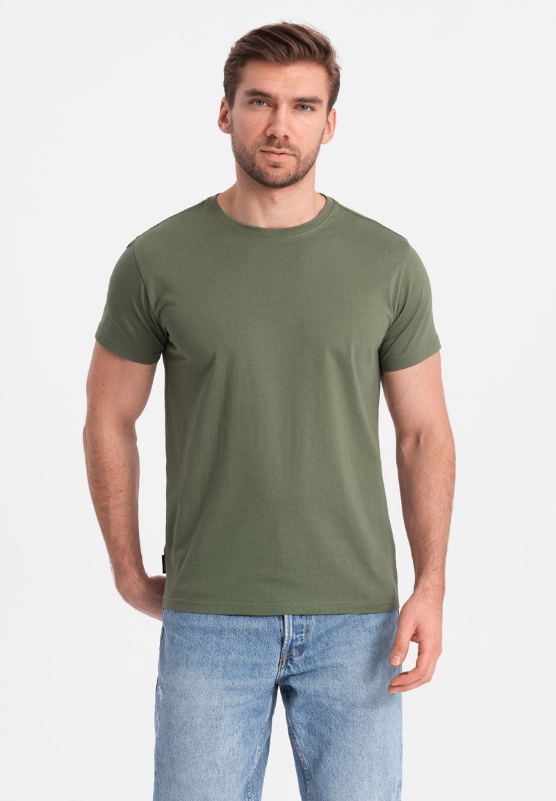 Oliven grøn bomulds t-shirt med rund hals, korte ærmer og en tapered silhuet, parret med lyseblå jeans.