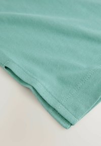 Tessuto di cotone celeste leggero, con una trama liscia, caratterizzato da orli cuciti con cura e un bordo piegato, che mostra semplicità nel design.