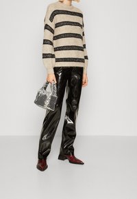 Beige stickad tröja med svarta ränder, glansiga svarta läderbyxor och en liten glittrig silverhandväska. Röda ankelkängor fulländar looken.