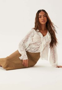Blouse en dentelle blanche avec un col froncé et des manches longues, associée à une jupe midi beige ajustée. Textures lisses, design élégant.